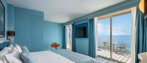 A hotel room with a bed, a chair, a small table, and a balcony with a view of the sea.