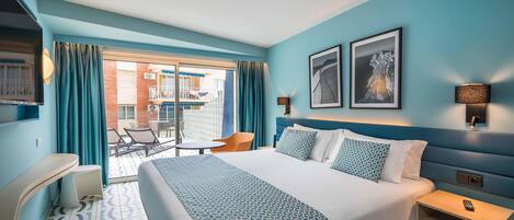 A hotel room with a bed, a desk, a chair, and a balcony with a view of the building.