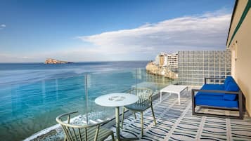 A balcony with a clear view of the sea, a white table, and a blue sofa.