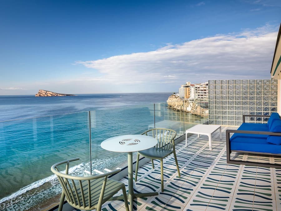 Un balcón con vistas despejadas al mar, una mesa blanca y un sofá azul.