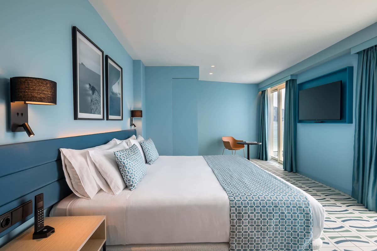 A modern hotel room with a large bed, a desk, and a TV.
