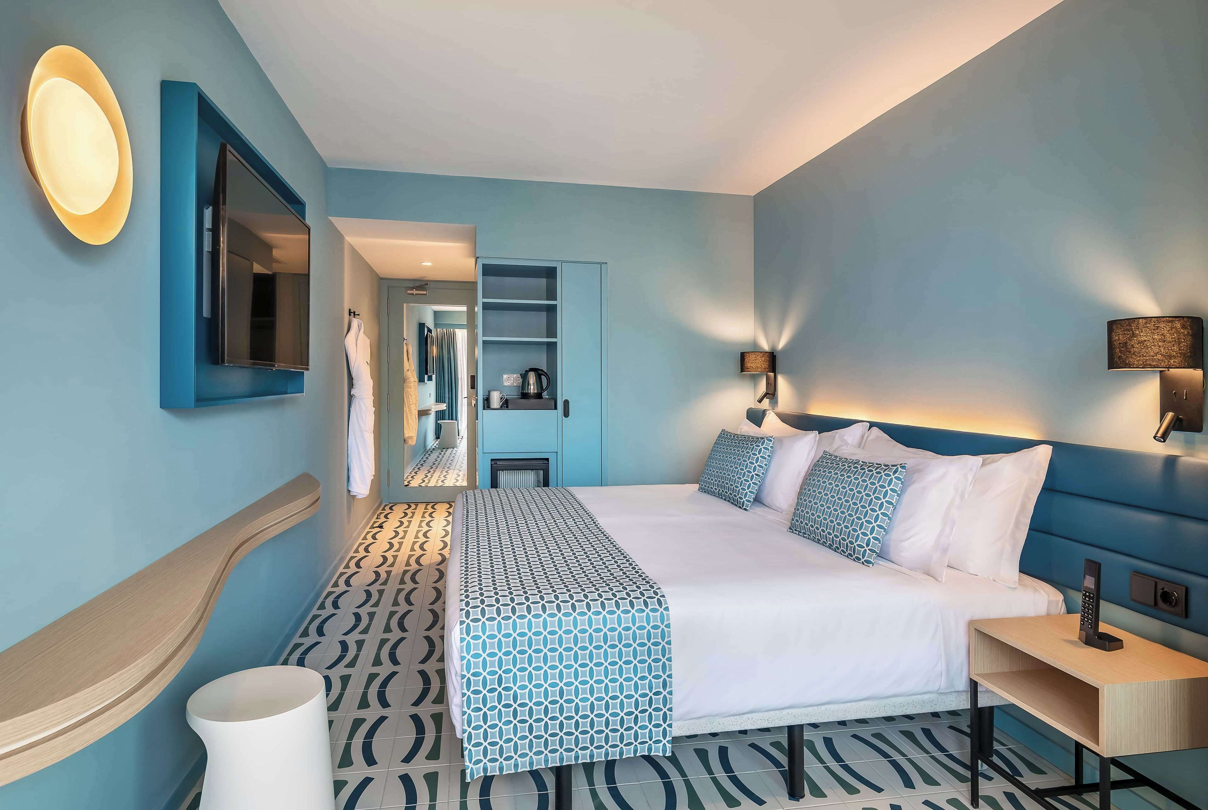 Ein modernes Hotelzimmer mit einem großen Bett, einem Nachttisch, einem Spiegel und einem Kleiderschrank.