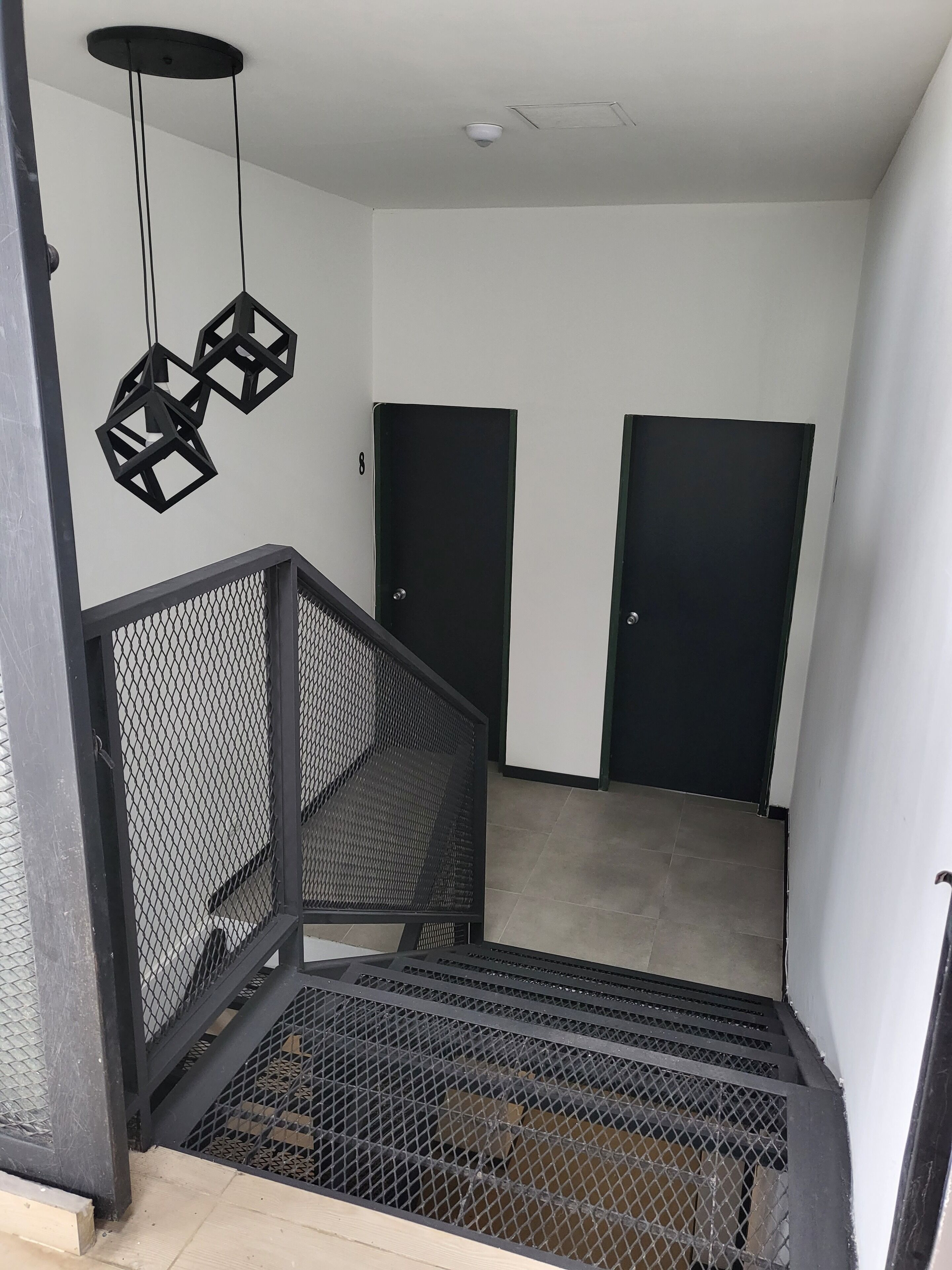 Un interior moderno con una escalera, puertas negras y una lámpara en el techo.