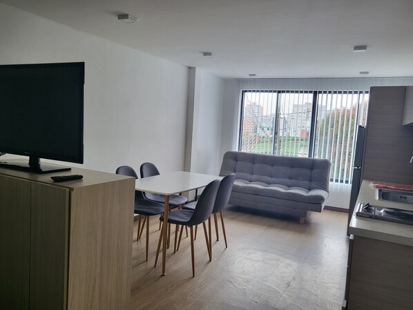 A modern living room with a flat-screen TV, a grey sofa, and a dining area with a table and chairs. - Casa Azul (Manizales)