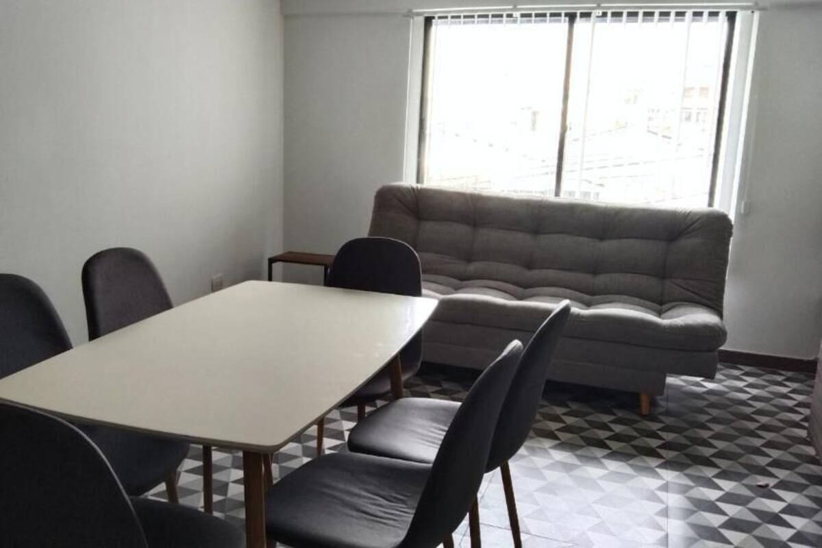 A room with a dining table and four chairs, a sofa, and a patterned floor.