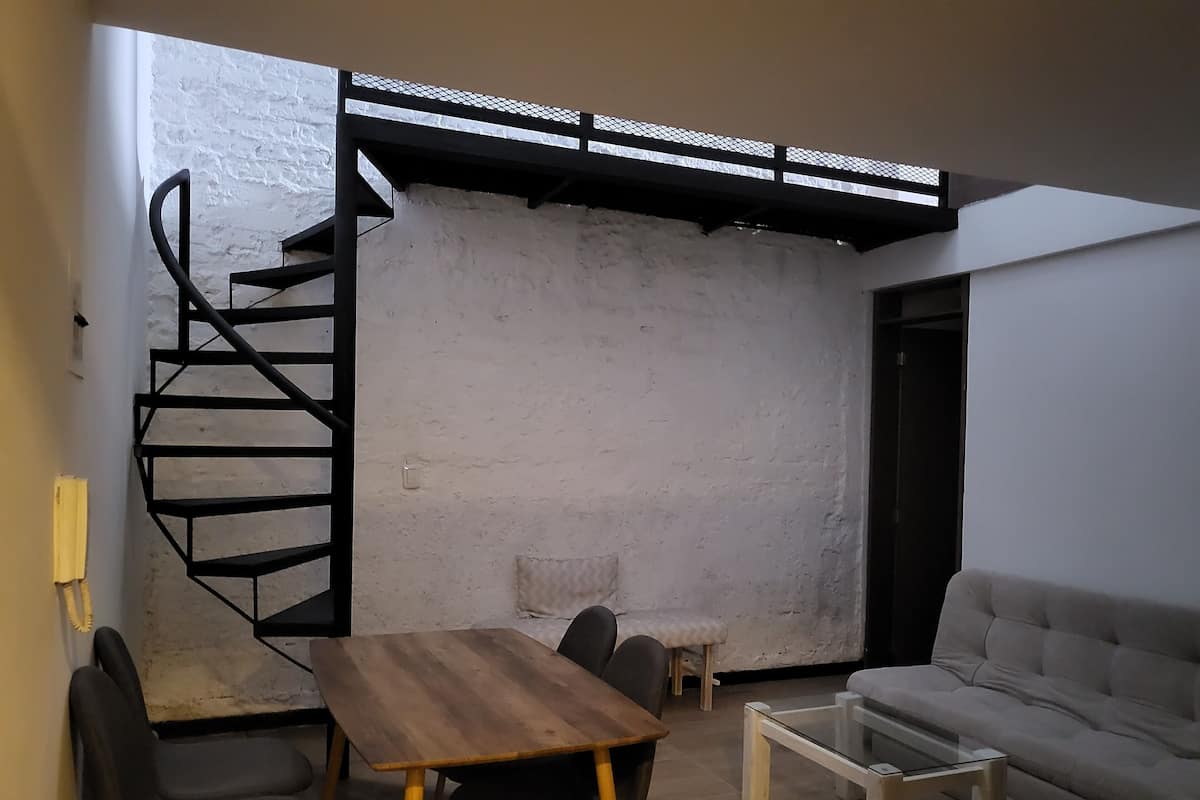 A room with a spiral staircase, a wooden table with chairs, a glass coffee table, and a grey sofa.