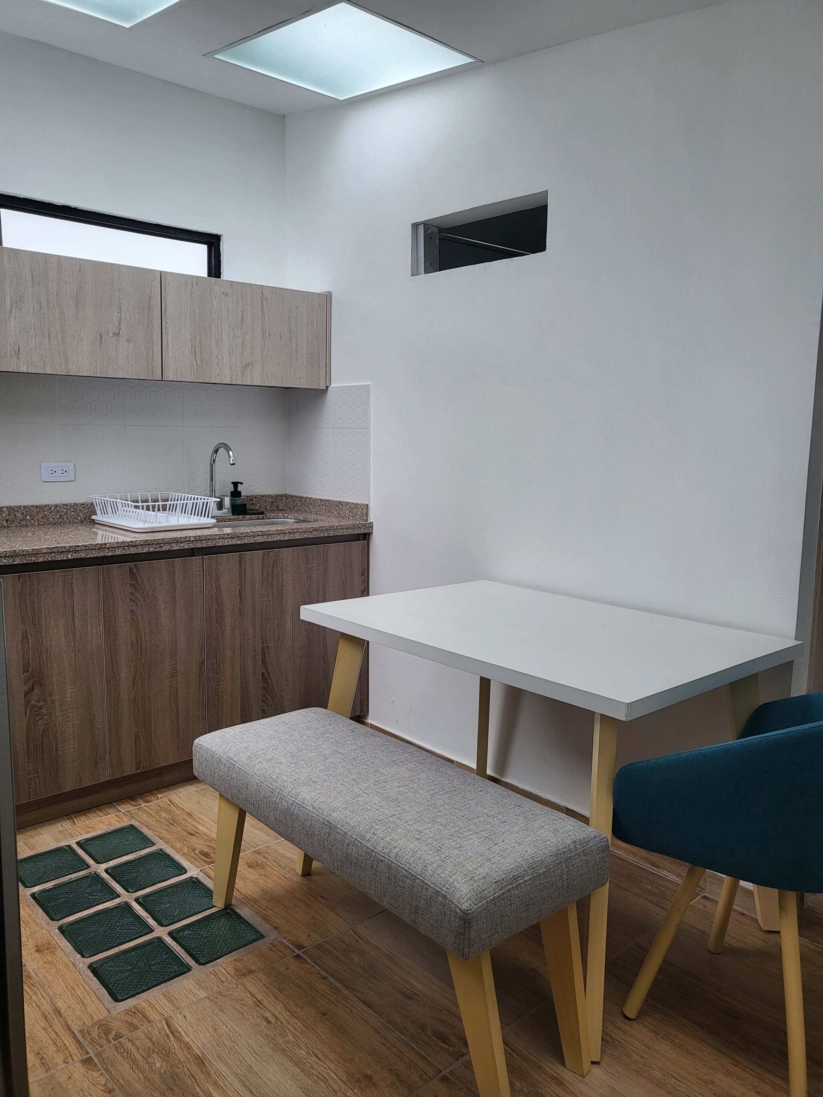 Una kitchenette compacta con un lavamanos integrado, un banco pequeño y una mesa blanca.