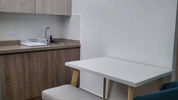 Una kitchenette compacta con un lavamanos integrado, un banco pequeño y una mesa blanca.