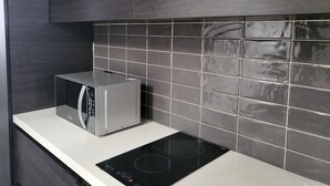Una cocina moderna con microondas integrado, placa de inducción negra y salpicadero de azulejos gris oscuro.
