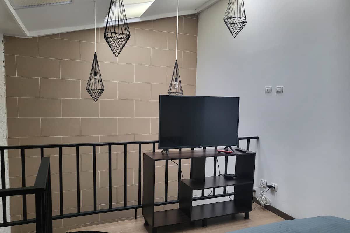 A modern room with a TV on a black stand, a bed, a small table, and hanging pendant lights.