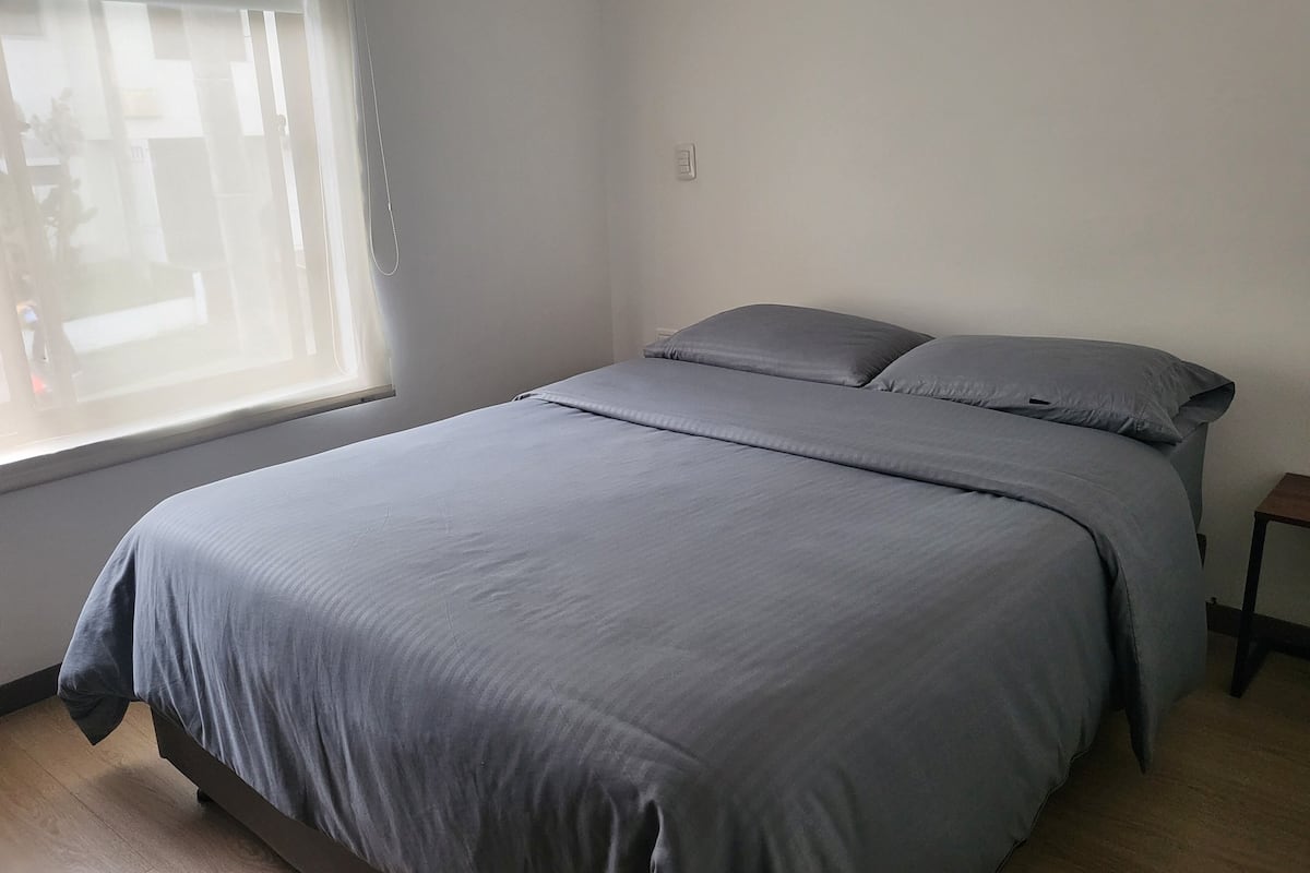 A bedroom with a bed, a nightstand, and a window.
