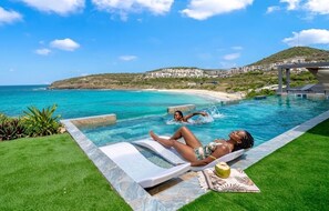 A pool with a view of the sea, a lounge area, and a hill with buildings in the background. - Condostmaarten panoramic (Adults Only) (Sint Maarten)