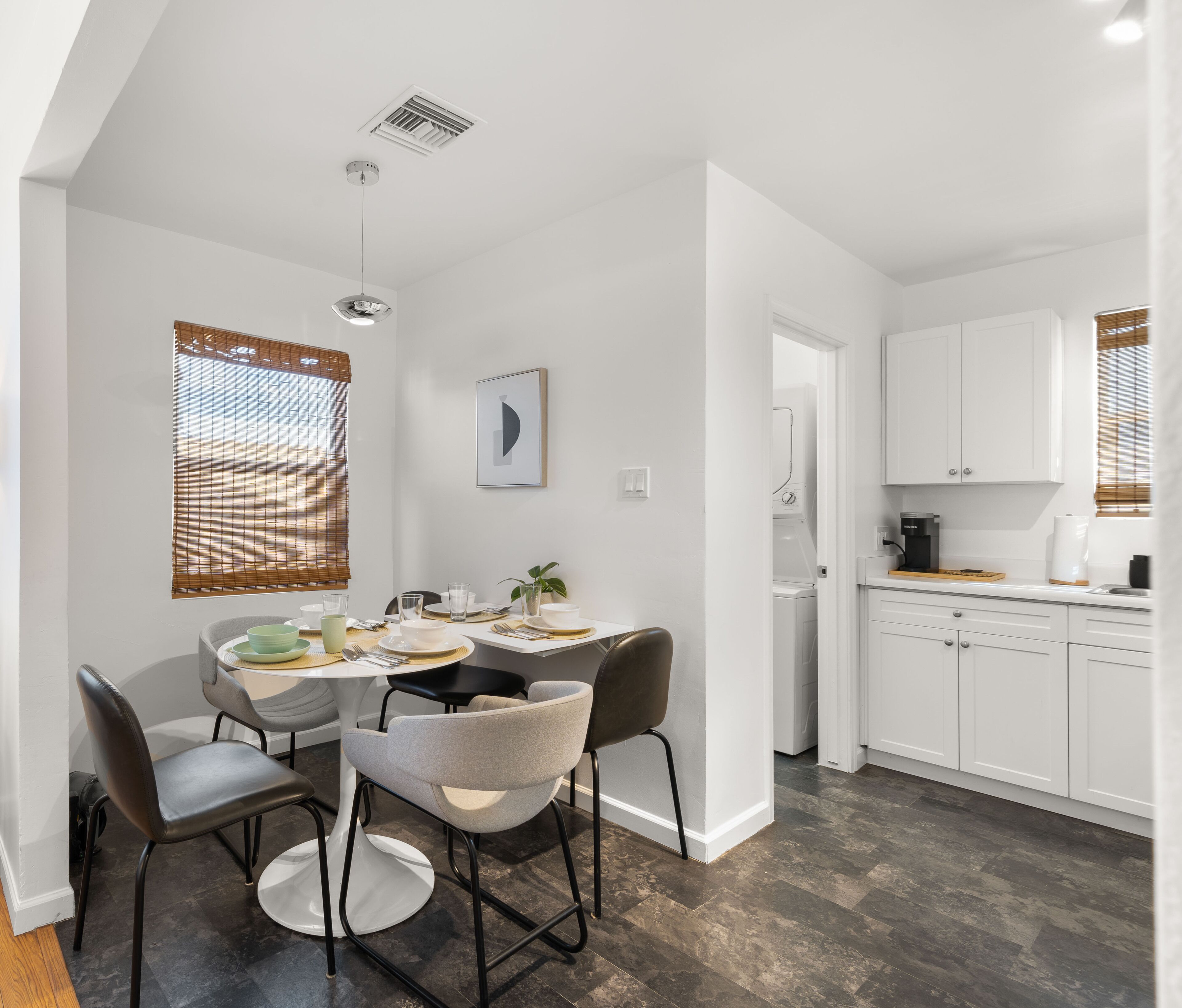 A modern kitchen with white cabinets, a dining area with a round table and chairs, and a visible dishwasher.