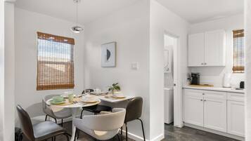A modern kitchen with white cabinets, a dining area with a round table and chairs, and a visible dishwasher.
