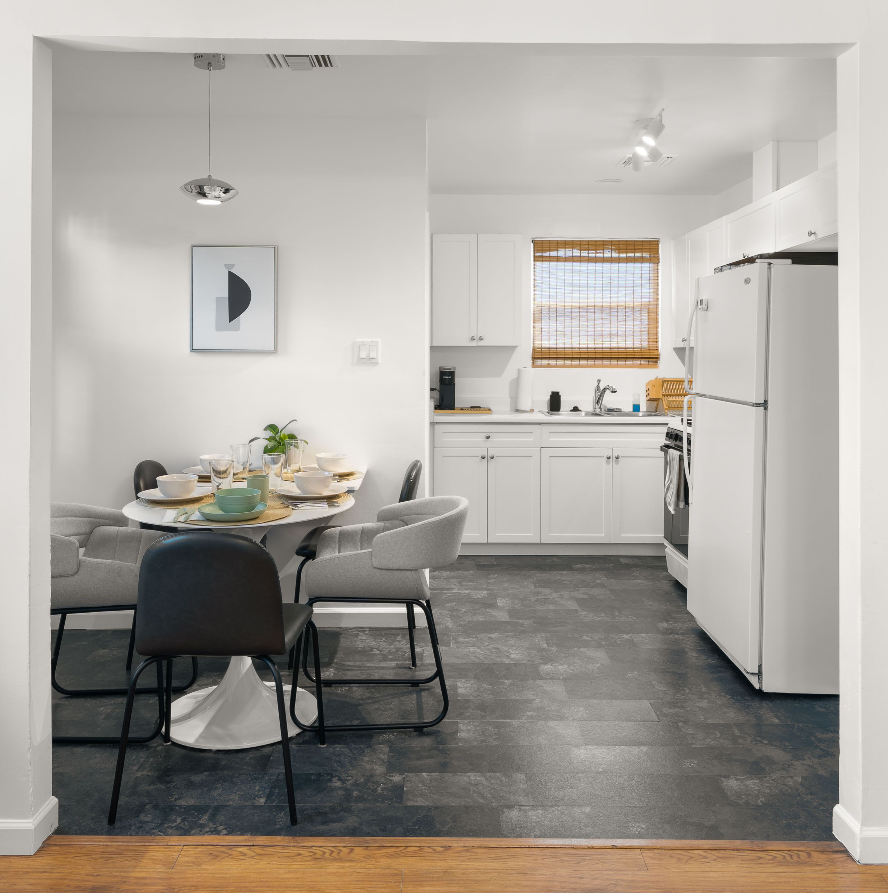 A modern kitchen with white cabinets, a dining table with chairs, a refrigerator, and a window with blinds.