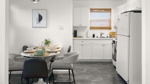 A modern kitchen with white cabinets, a dining table with chairs, a refrigerator, and a window with blinds. - Central Phx Kid/Pet friendly home next to Banner Hospital & Historic Coronado (Phoenix)