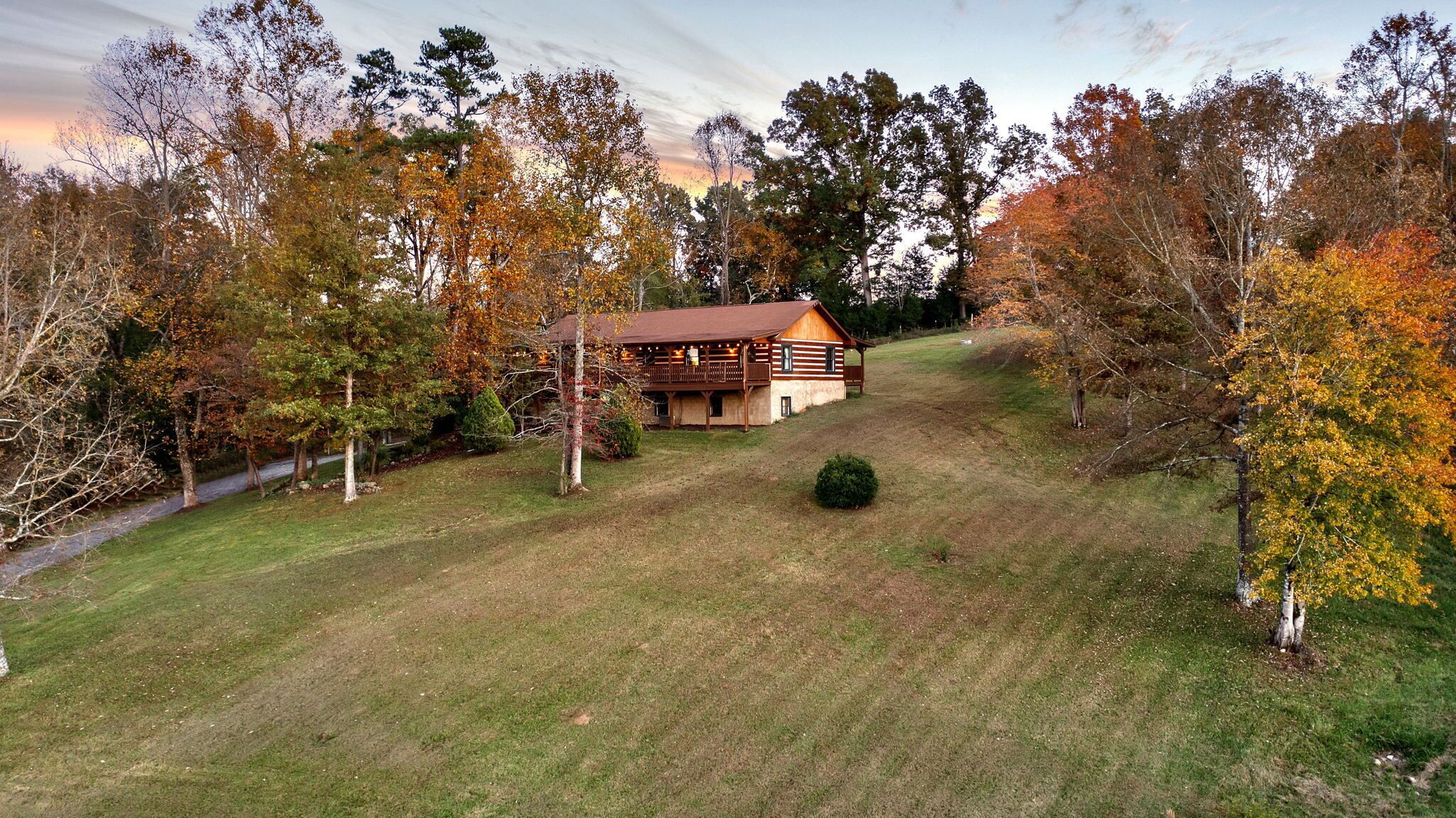 A log cabin with a deck, surrounded by a grassy area and trees with autumn foliage.