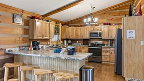 A kitchen with wooden cabinets, a central island with stools, stainless steel appliances, and a hanging light fixture. - Private log cabin for 16 (Cleveland)