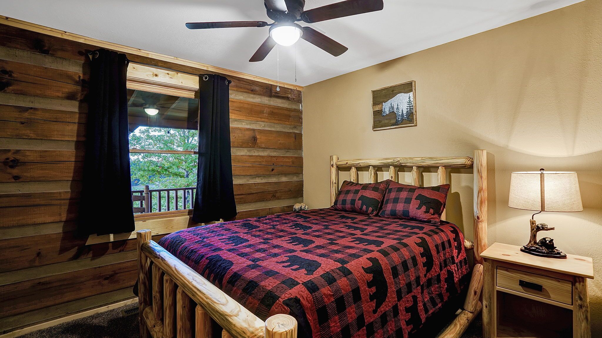 Un dormitorio con cabecera de madera, cama con colcha estampada, mesita de noche con lámpara y ventilador de techo.