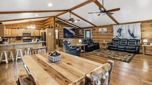 A spacious living area with a wooden dining table, black leather sofas, and a ceiling fan. - Private log cabin for 16 (Cleveland)
