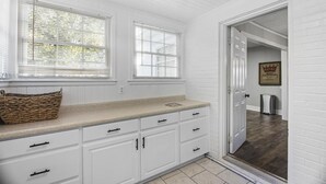 A kitchen with white cabinetry, a beige countertop, and two windows with blinds. - Forest Hills Cottage - 4.2 Miles from Masters (Augusta)