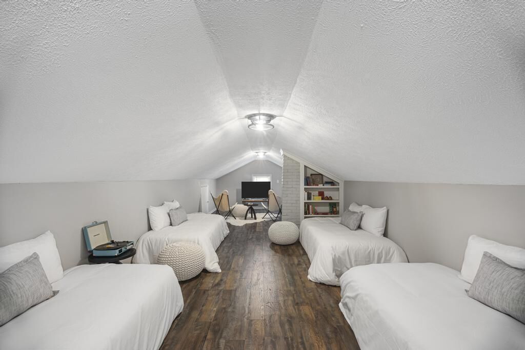 A cozy attic bedroom with two beds, a TV, and a bookshelf.