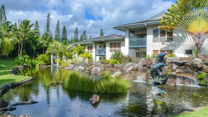 A hotel with a pond, palm trees, and a waterfall.