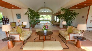 A spacious lobby with a central round table, two sofas, and a bench. There are potted plants and lamps around the seating area.