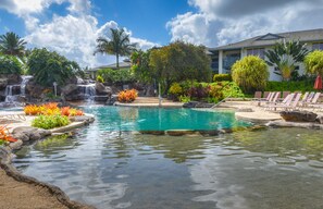 A pool with a waterfall, surrounded by tropical plants and a building with a balcony. - 2Br/2Ba in beautiful Kauai! Bali Hai Villas, pool, hot tub, AC! (Princeville)