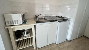 Une cuisine compacte avec des meubles blancs, un four à micro-ondes, un évier et un petit réfrigérateur.