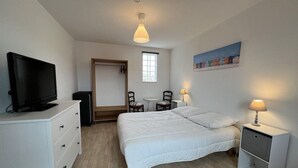 Une chambre à coucher avec un lit, une télévision, un bureau, une chaise, une lampe et un tableau au mur.