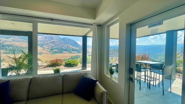 A room with a sofa facing a sliding glass door leading to an outdoor patio. The room has a view of a mountainous landscape. - 
Oasis @ Black Mountain - Only 25 mins to Big White (Kelowna)