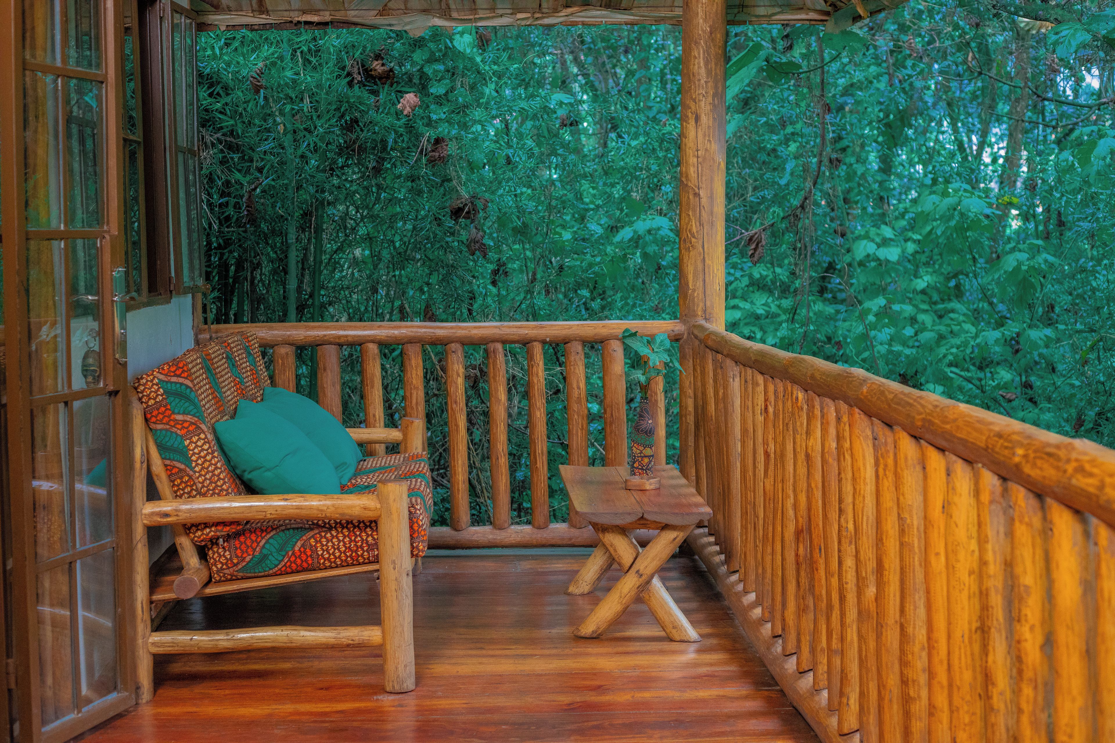 A wooden deck with a bench and a small table, surrounded by dense green foliage.