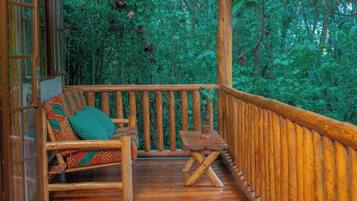 Una terraza de madera con un banco y una mesita, rodeada de abundante follaje verde.