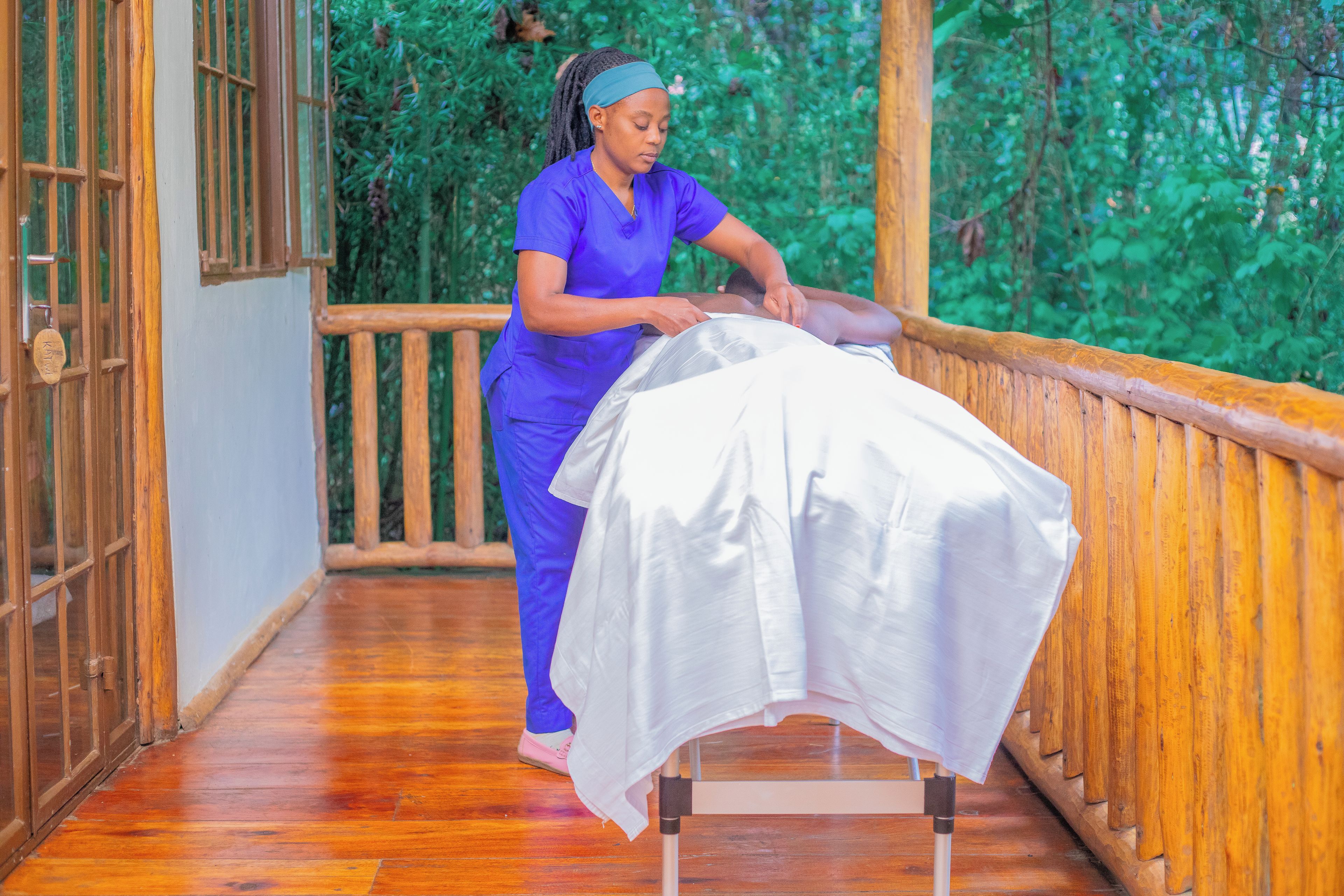 A massage therapy session in a wooden-floored room with a view of greenery outside.