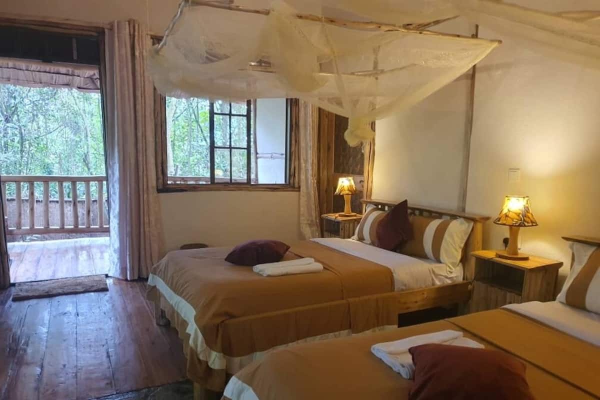 A room with two beds, wooden floors, a window with curtains, and a balcony.
