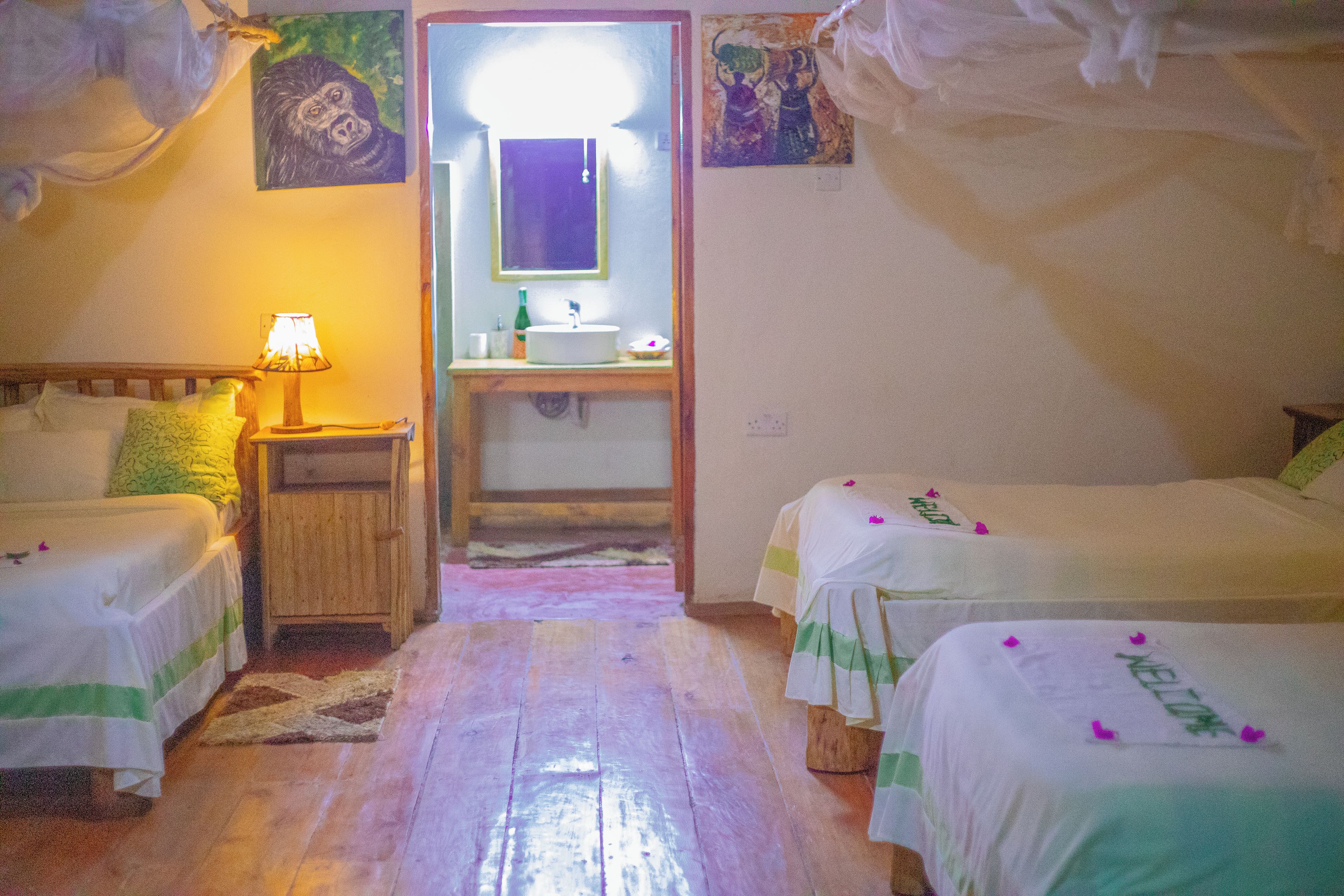 Una habitación con dos camas, una mesita de noche con lámpara, un baño con lavamanos y espejo.