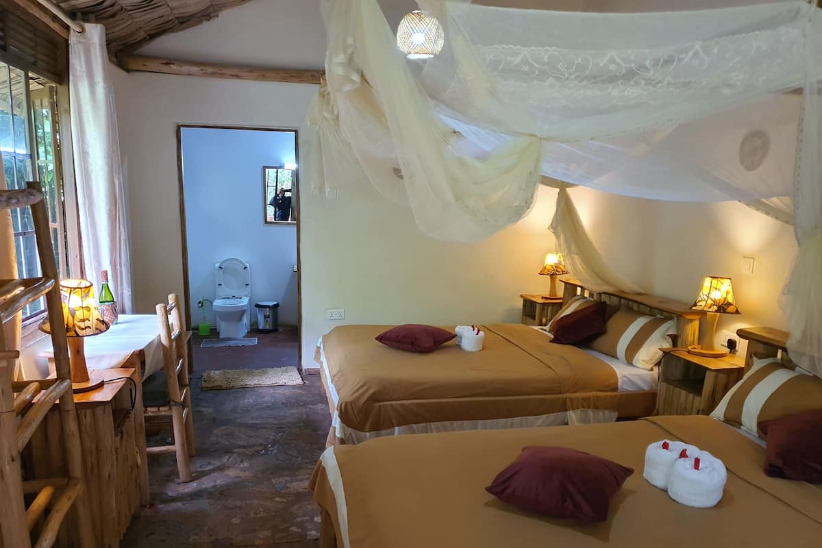 A room with two beds, wooden furniture, a table with a lamp, and a window with curtains.