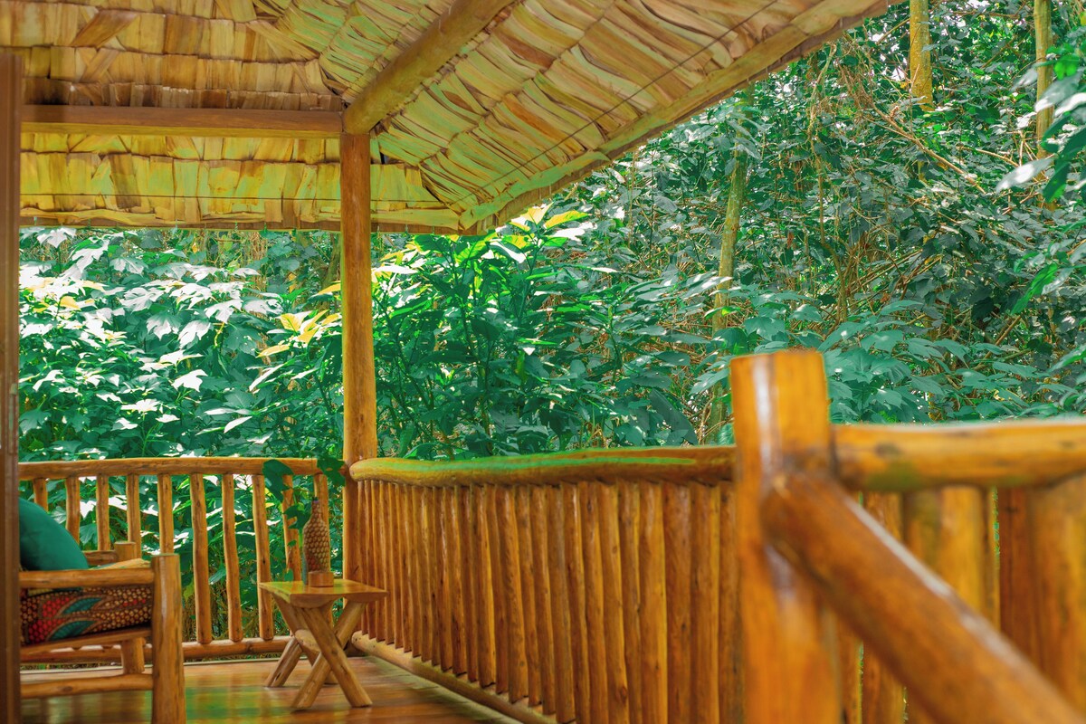 A wooden deck with a thatched roof, surrounded by lush greenery.