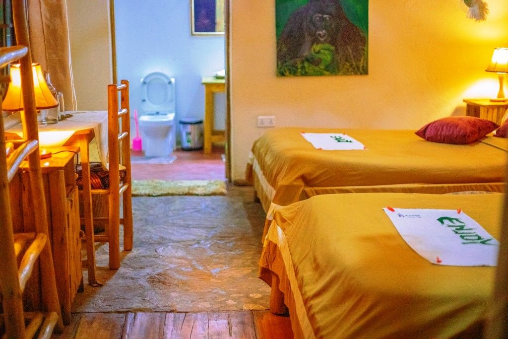 A room with two beds, a wooden chair, a table with a lamp, and a painting on the wall.