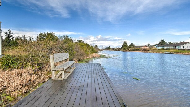 A wooden deck extending over a calm river, with a bench and dense vegetation on one side. - Canal-Front Vacation Rental in Ocean Shores (Ocean Shores)
