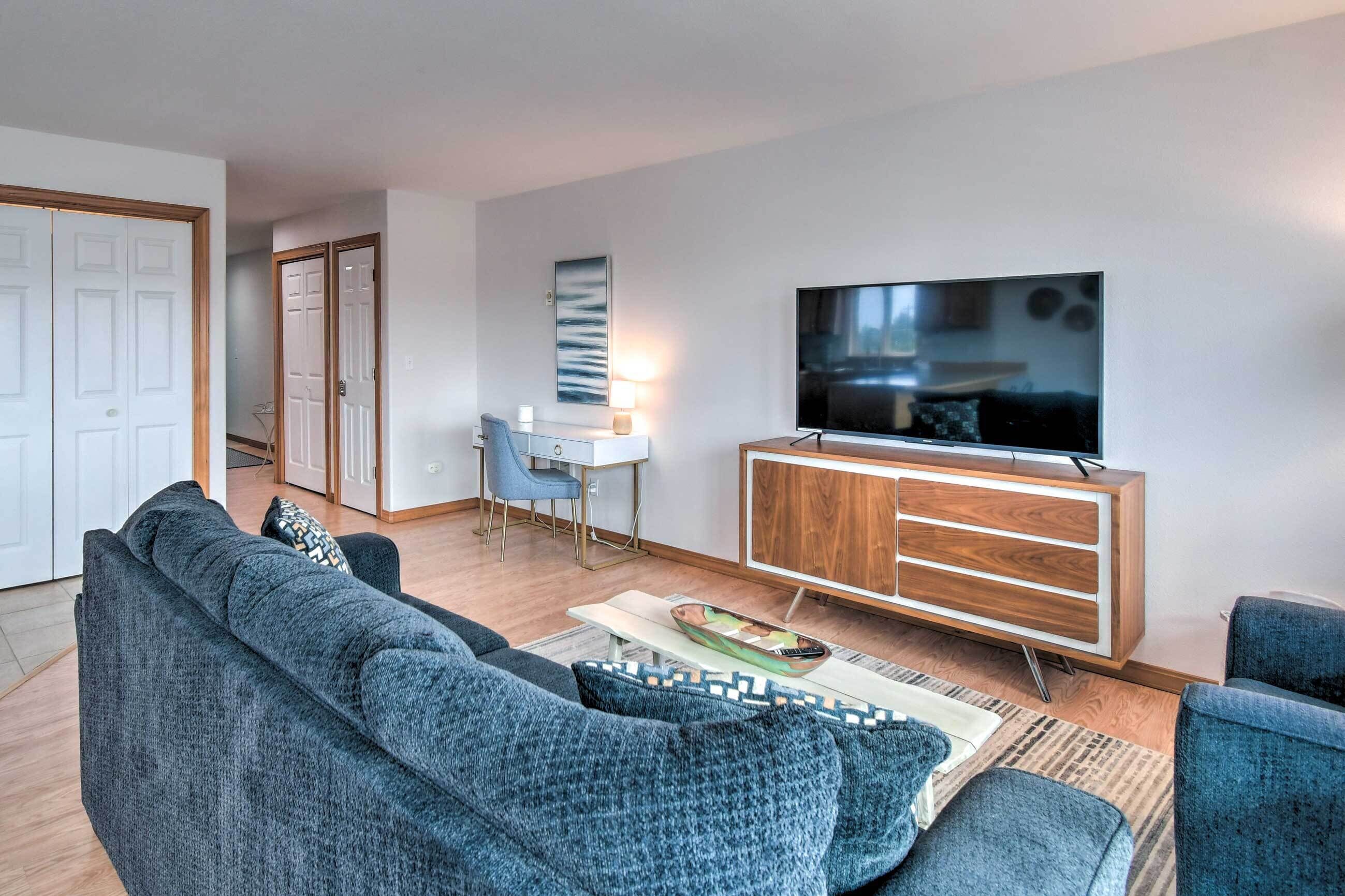 Un salon moderne avec un canapé gris, un meuble en bois, un téléviseur à écran plat et un coin repas comprenant une table et des chaises.
