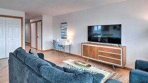 A modern living room with a grey sofa, a wooden cabinet, a flat-screen TV, and a dining area with a table and chairs. - Canal-Front Vacation Rental in Ocean Shores (Ocean Shores)