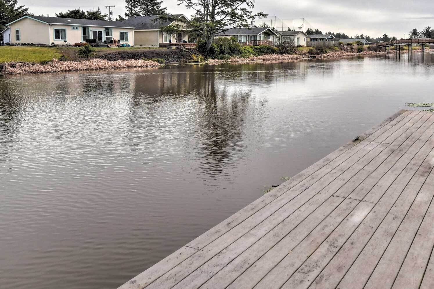 Un lac paisible avec un quai en bois, entouré de maisons et d’un pont.