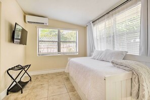 A bedroom with a bed, a TV mounted on the wall, and a window with blinds. - Vacation Rental w/ Private Pool in Wilton Manors (Wilton Manors)