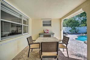 A patio area with a table and chairs, a small window, and a view of a backyard with a pool. - Vacation Rental w/ Private Pool in Wilton Manors (Wilton Manors)