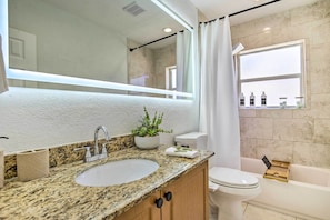 A bathroom with a granite countertop sink, a white toilet, a bathtub, and a large mirror. - Vacation Rental w/ Private Pool in Wilton Manors (Wilton Manors)