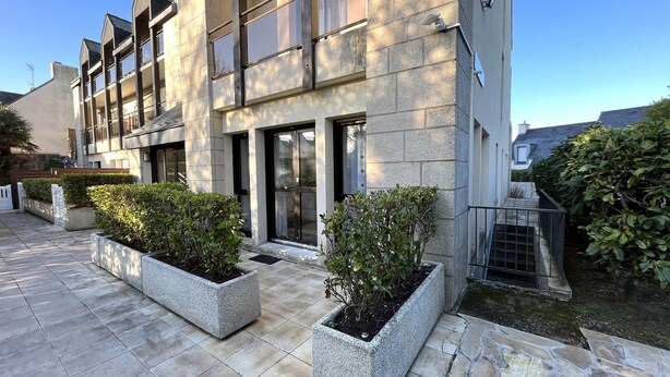 Un edificio moderno con fachada de piedra, ventanas amplias y un patio empedrado con jardineras.