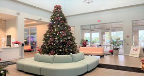 A Christmas tree in a lobby with a light-colored sofa and a reception desk.