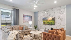 Un salon moderne avec un canapé, un fauteuil et un téléviseur fixés sur un mur en marbre.
